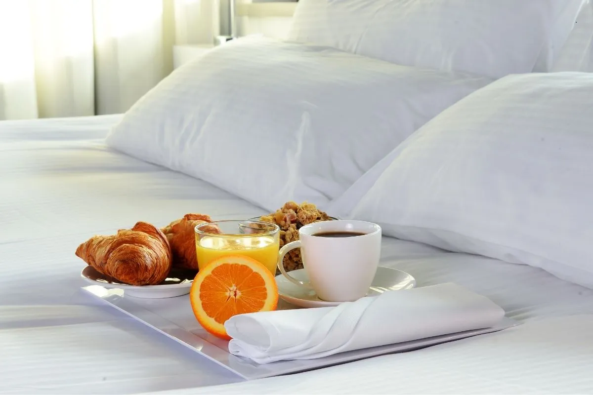 Vassoio con colazione, cornetti, succo d'arancia e caffè su un letto bianco