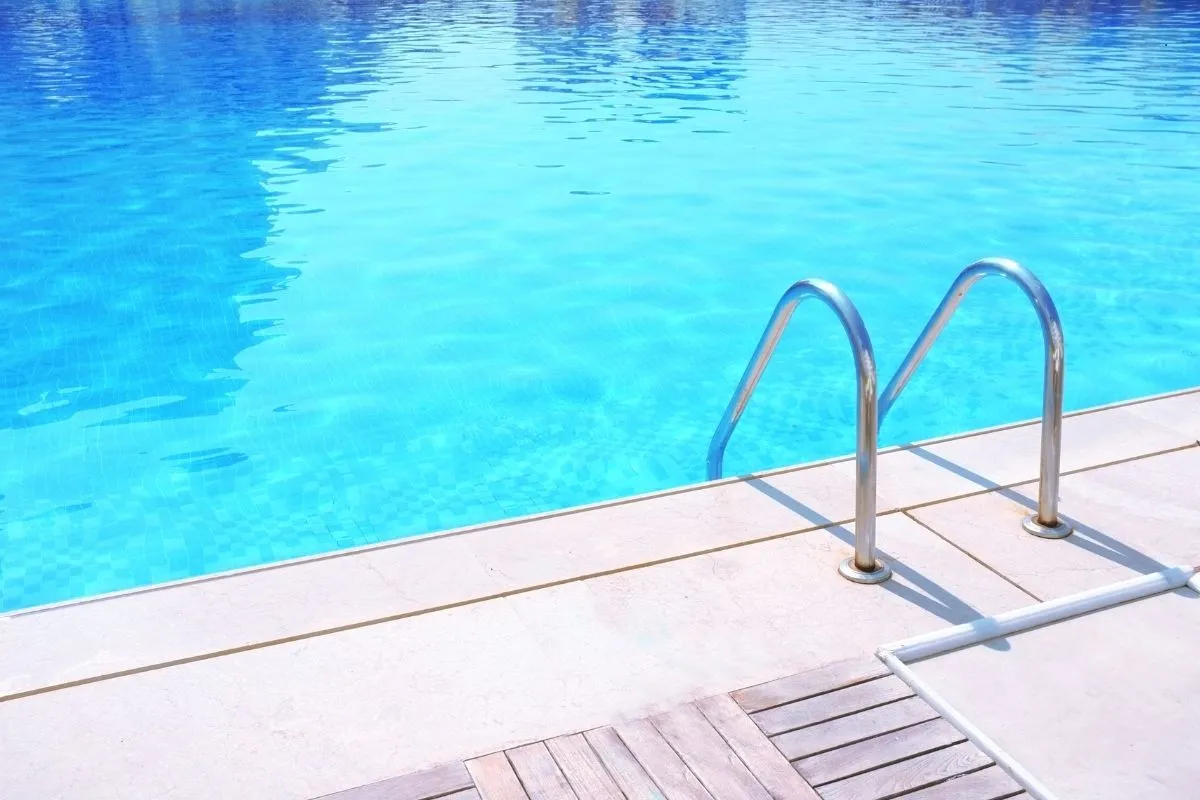 Bordo piscina con acqua azzurra cristallina e scaletta in acciaio