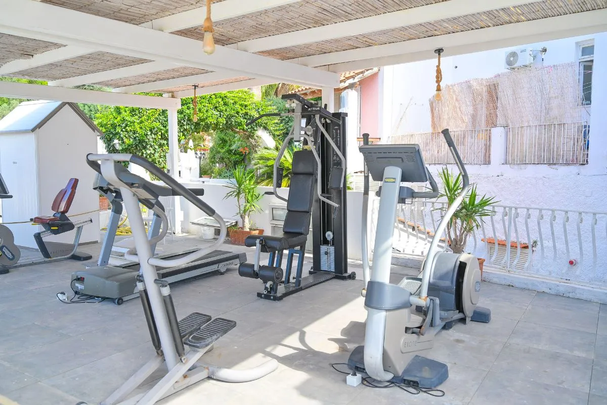 Palestra all'aperto coperta da pergolato con attrezzi cardio e macchine per pesi