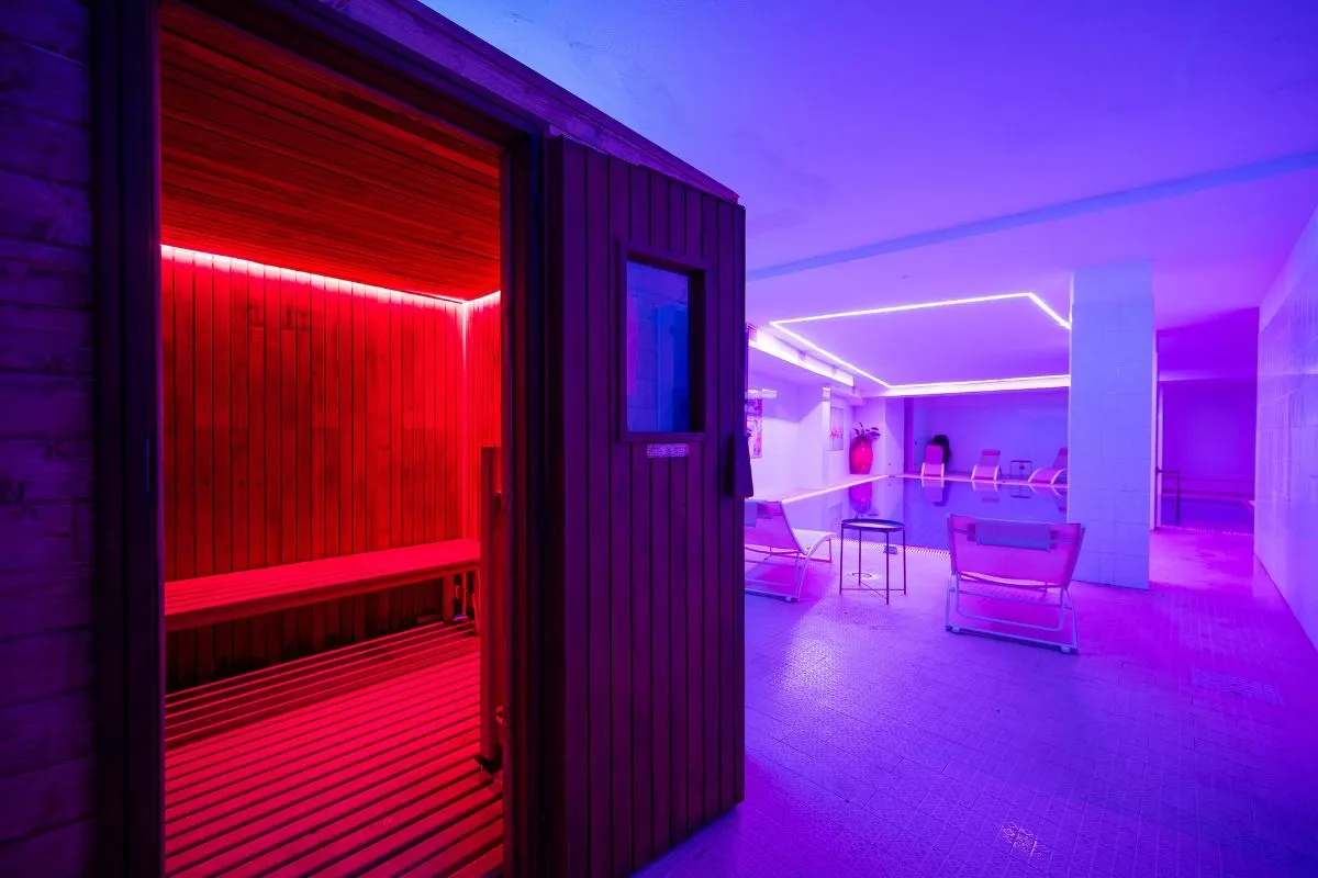Sauna in legno con luce rossa e zona relax della spa illuminata di viola