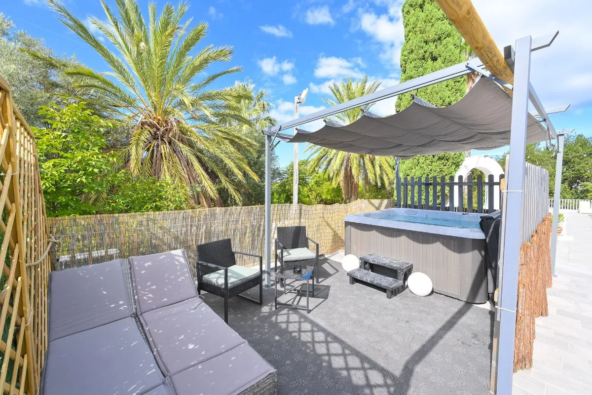 Terrazza privata con vasca idromassaggio, lettino e poltrone sotto pergola con palme