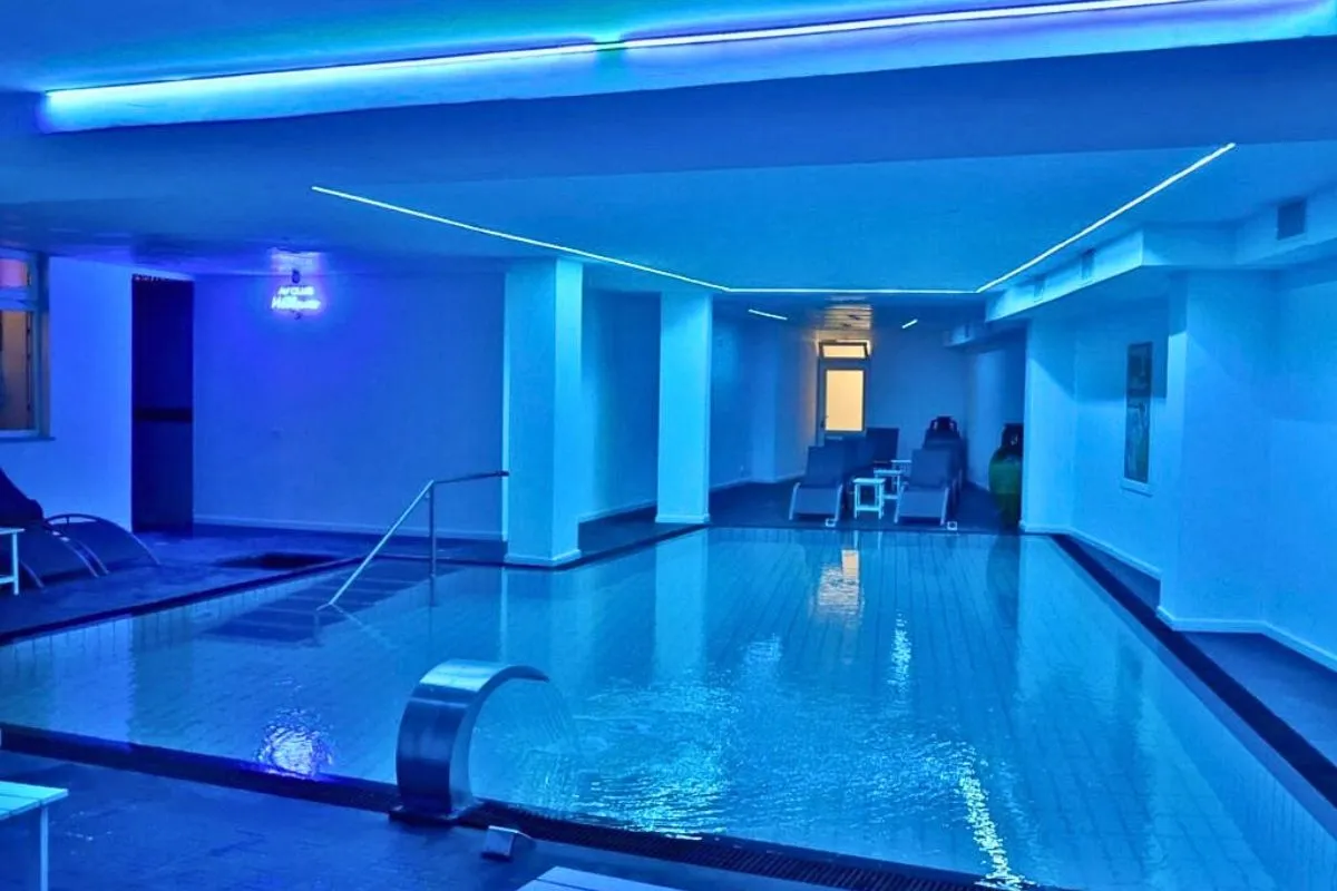 Piscina interna termale con luci blu, cascata d'acqua e lettini relax