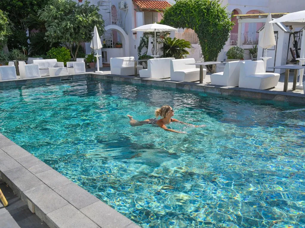 Una nuotata nella piscina esterna circondata da divanetti bianchi e vegetazione
