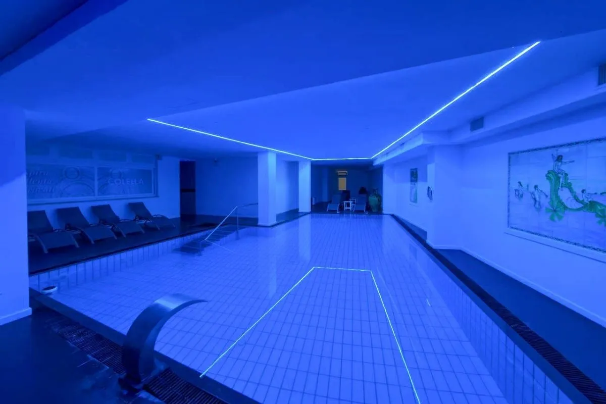 Piscina interna termale con illuminazione blu, cascata e dipinto a parete