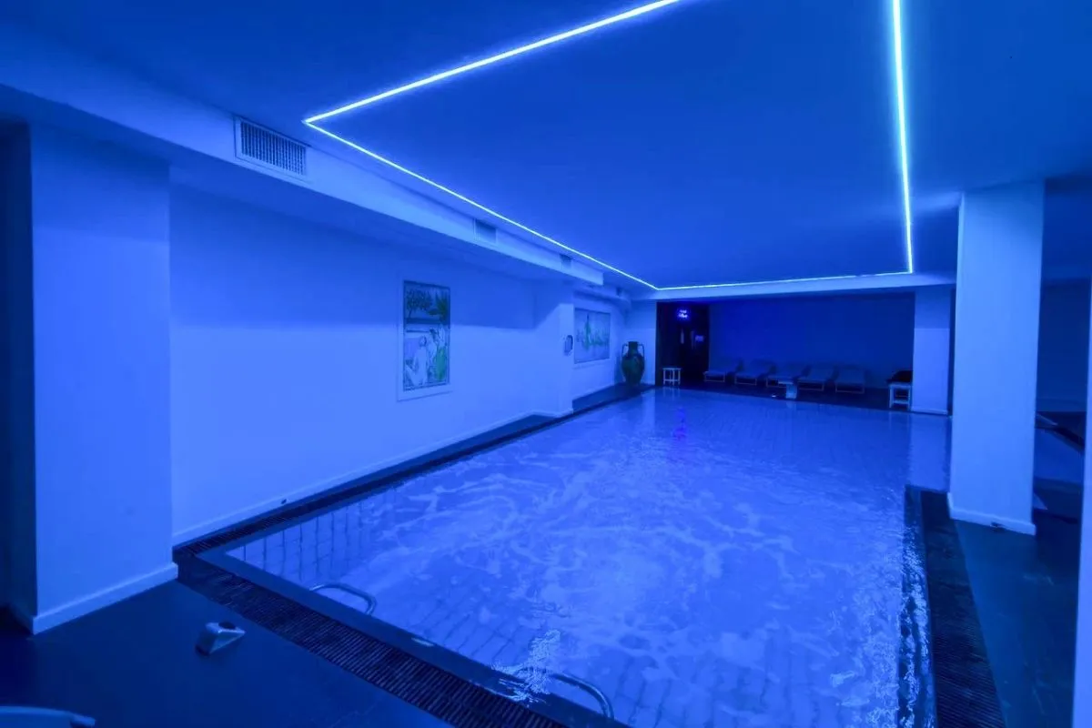 Piscina interna termale con luci blu, lettini e dettagli luminosi al soffitto