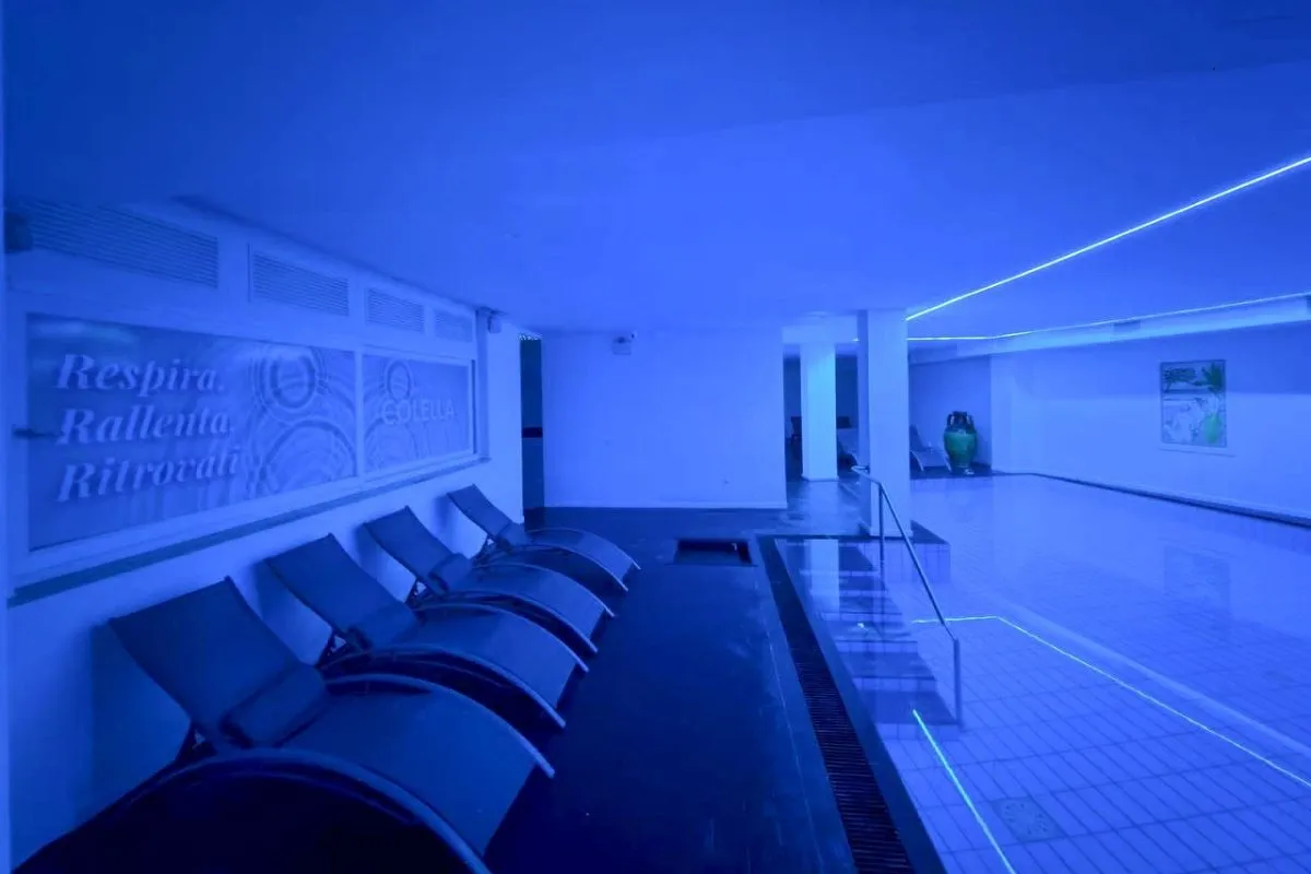 Piscina interna termale con illuminazione blu e lettini lungo la parete