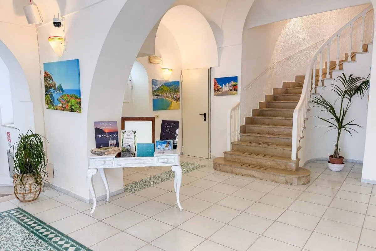 Hall dell'hotel con archi bianchi, scala e quadri colorati alle pareti
