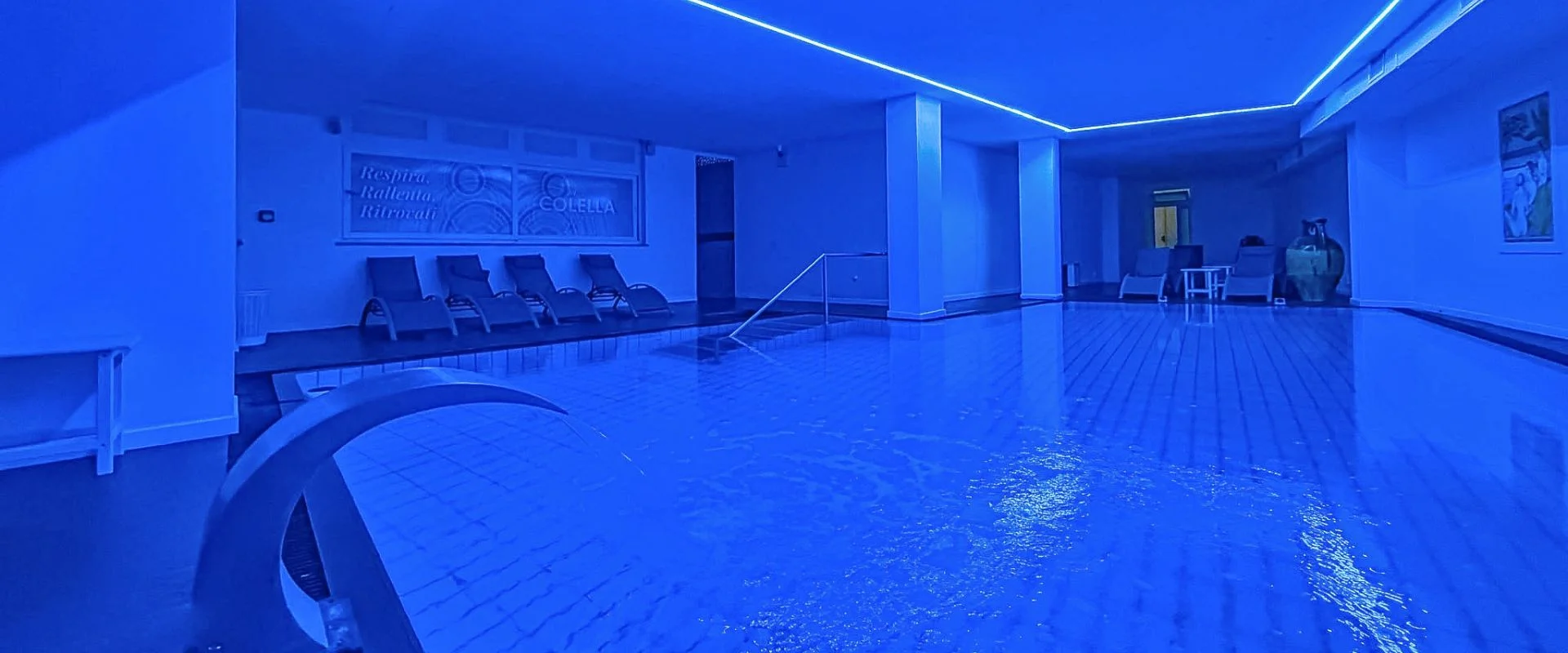 Piscina interna termale con illuminazione blu, lettini e cascata d'acqua