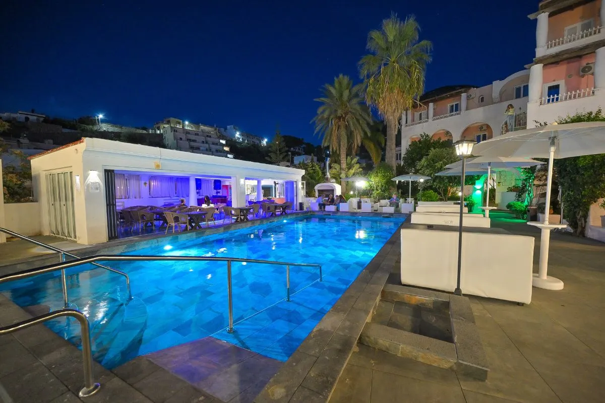 Piscina esterna di sera con illuminazione blu e zona ristorante coperta sullo sfondo