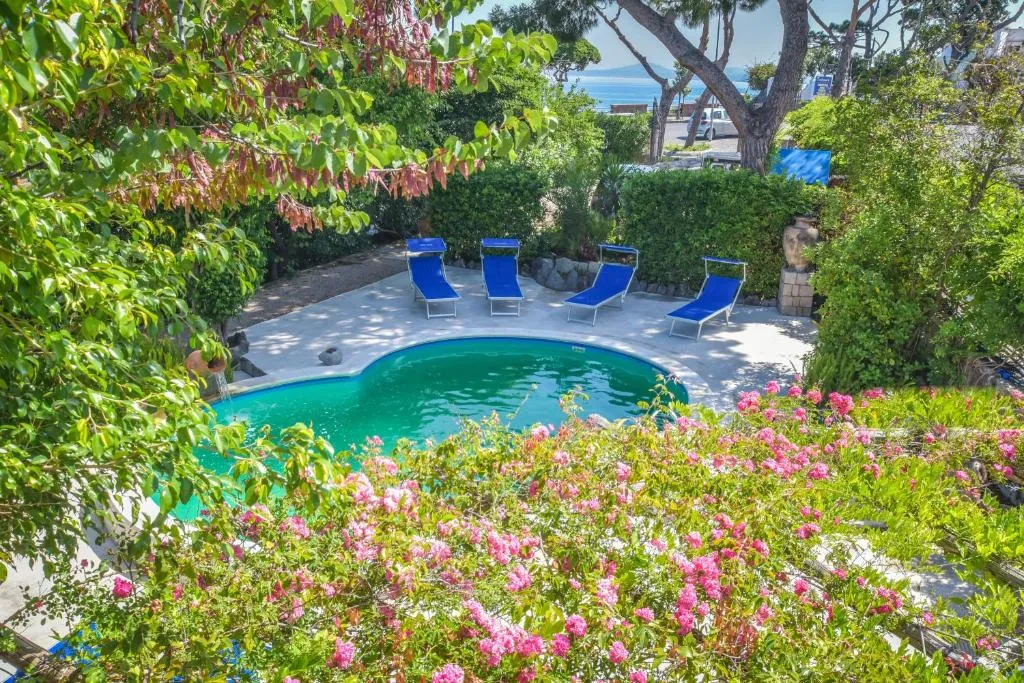 Piscina immersa nel giardino fiorito con lettini blu e vista mare
