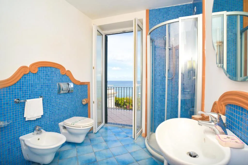 Bagno con piastrelle blu, doccia e porta affacciata sul balcone vista mare