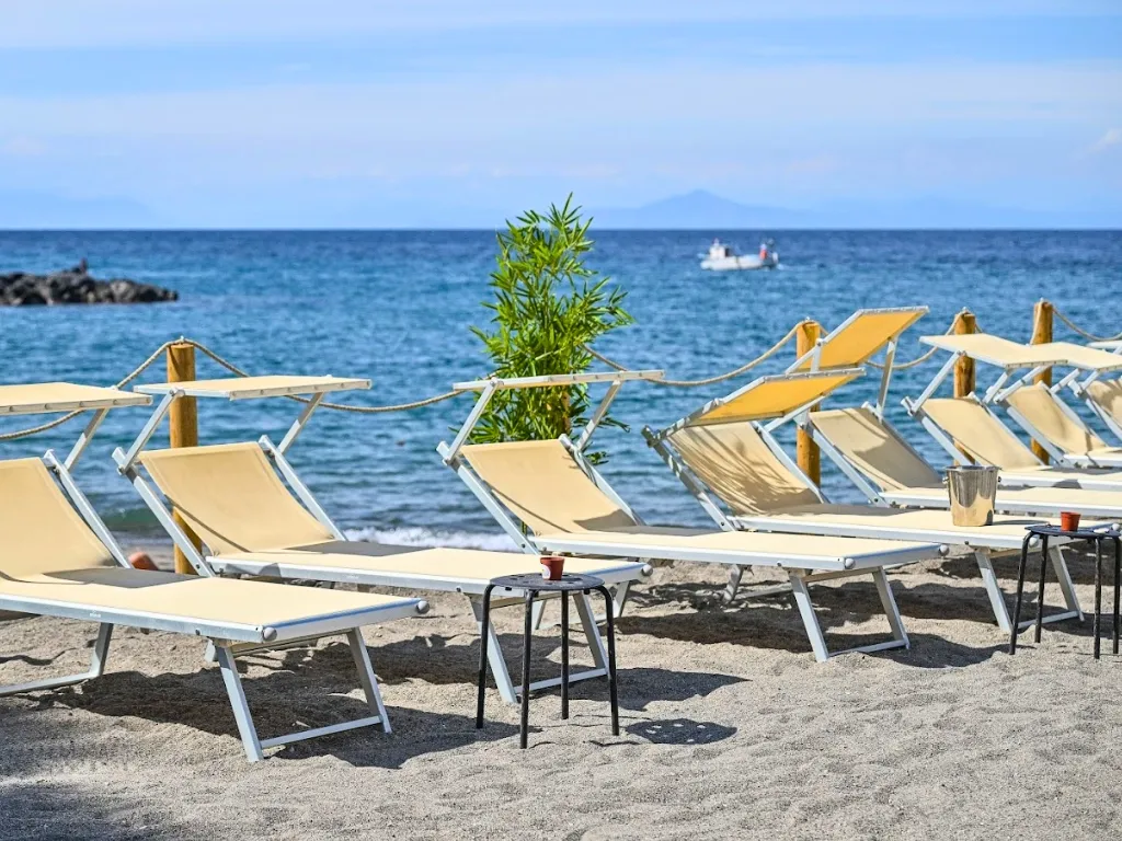 Lettini da spiaggia in tela beige con parasole sulla sabbia fronte mare e barca in lontananza