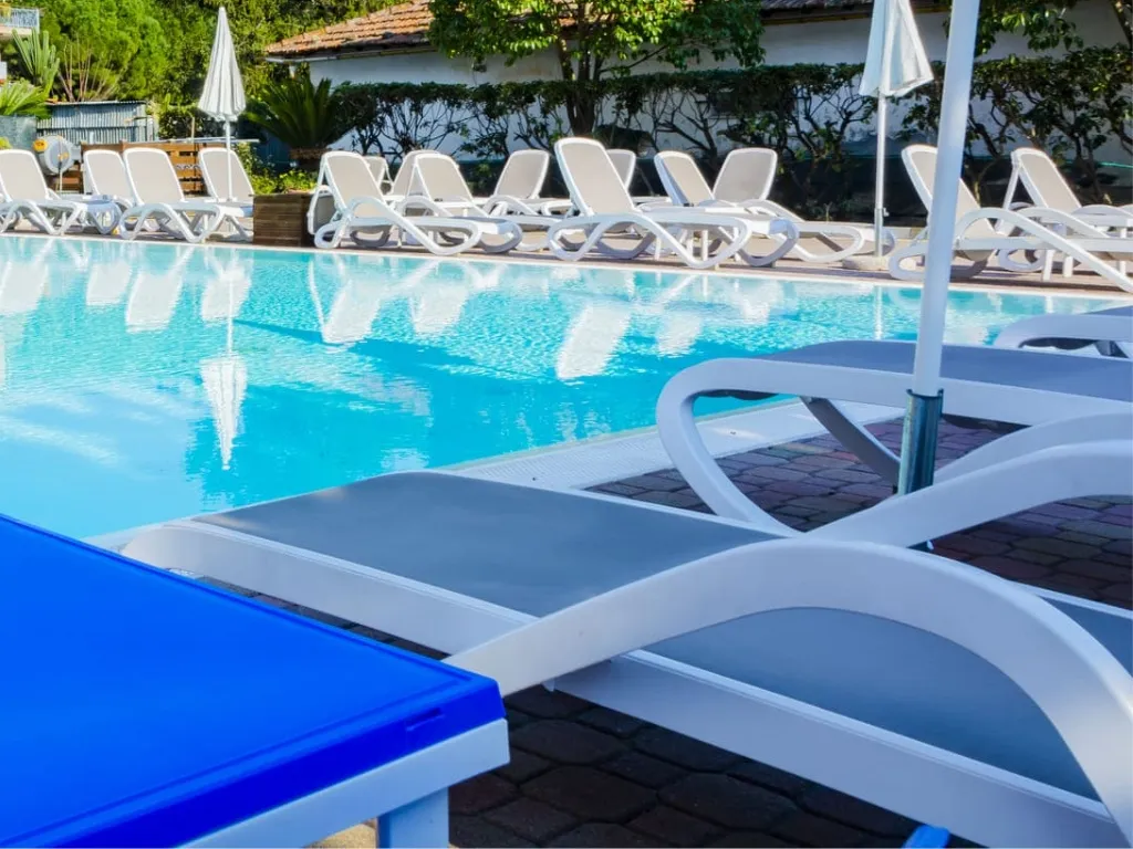Bordo piscina con lettini bianchi e ombrelloni circondati dal verde