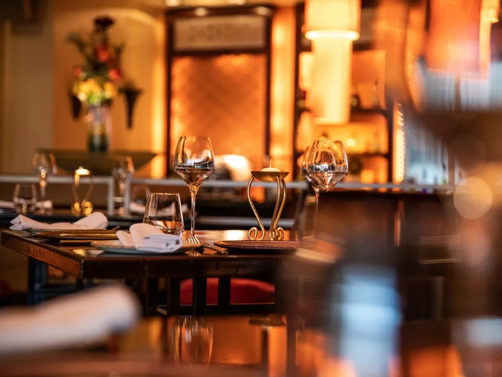 Tavolo di ristorante elegante apparecchiato con calici e candele in atmosfera calda e soffusa