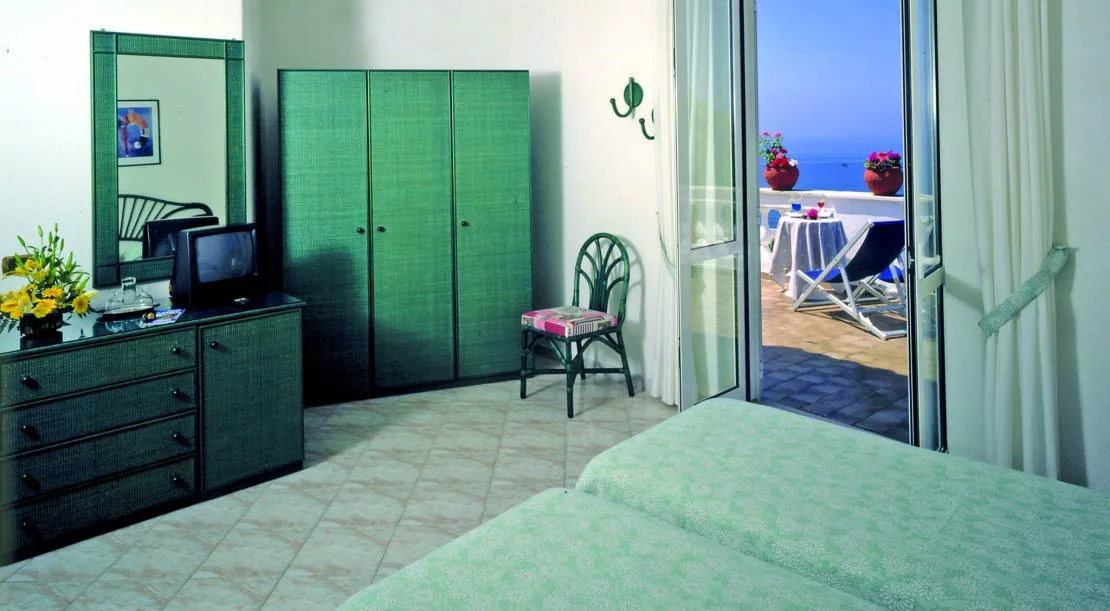Camera con mobili verdi in vimini e terrazza con vista sul mare