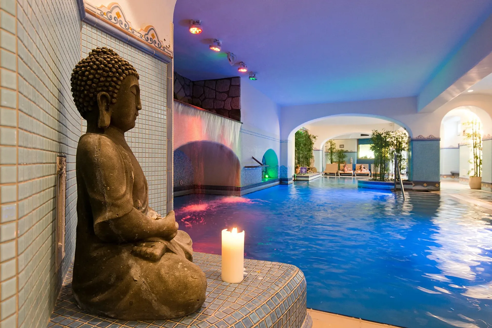 Percorso benessere interno con statua di Buddha, cascata e luci colorate nella zona spa
