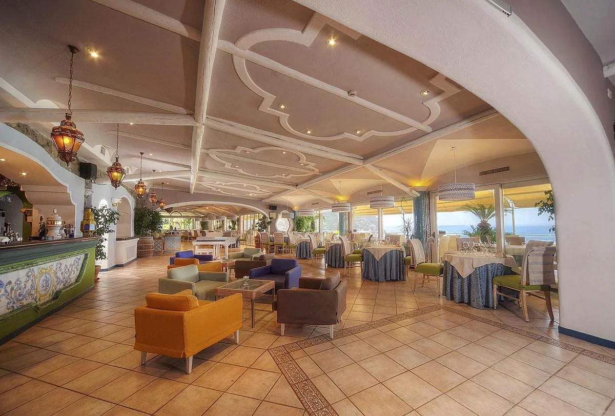 Sala ristorante con tavoli apparecchiati, poltrone colorate e vista sul mare