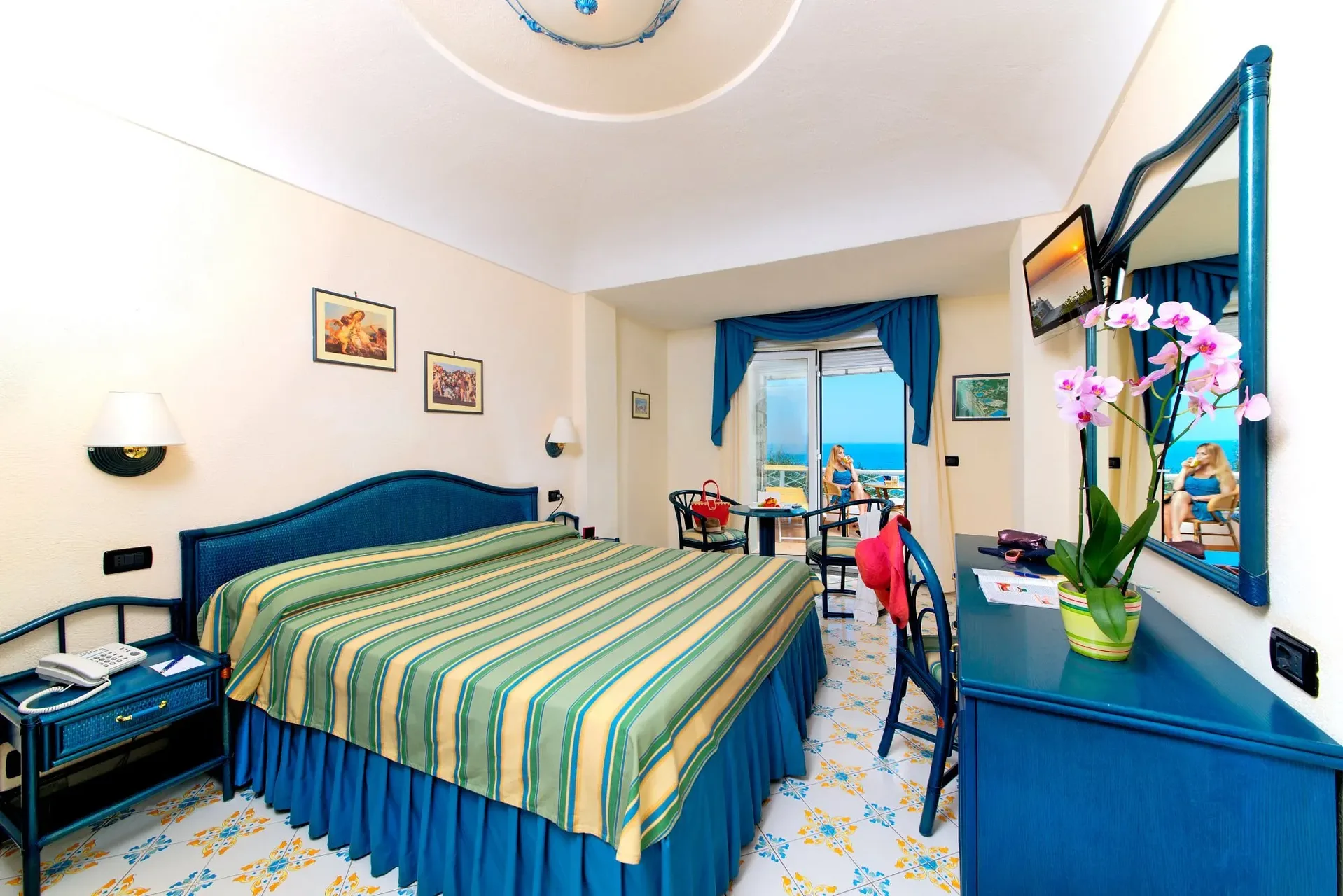 Camera doppia con copriletto a righe verdi, arredi blu e balcone vista mare
