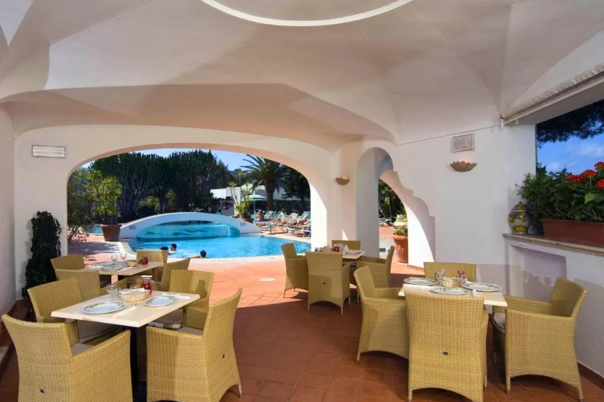 Terrazza ristorante coperta con tavoli apparecchiati e poltrone in vimini affacciata sulla piscina
