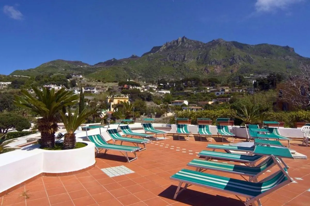 Terrazza solarium in cotto con lettini a righe verdi e vista sulle montagne verdi dell'isola
