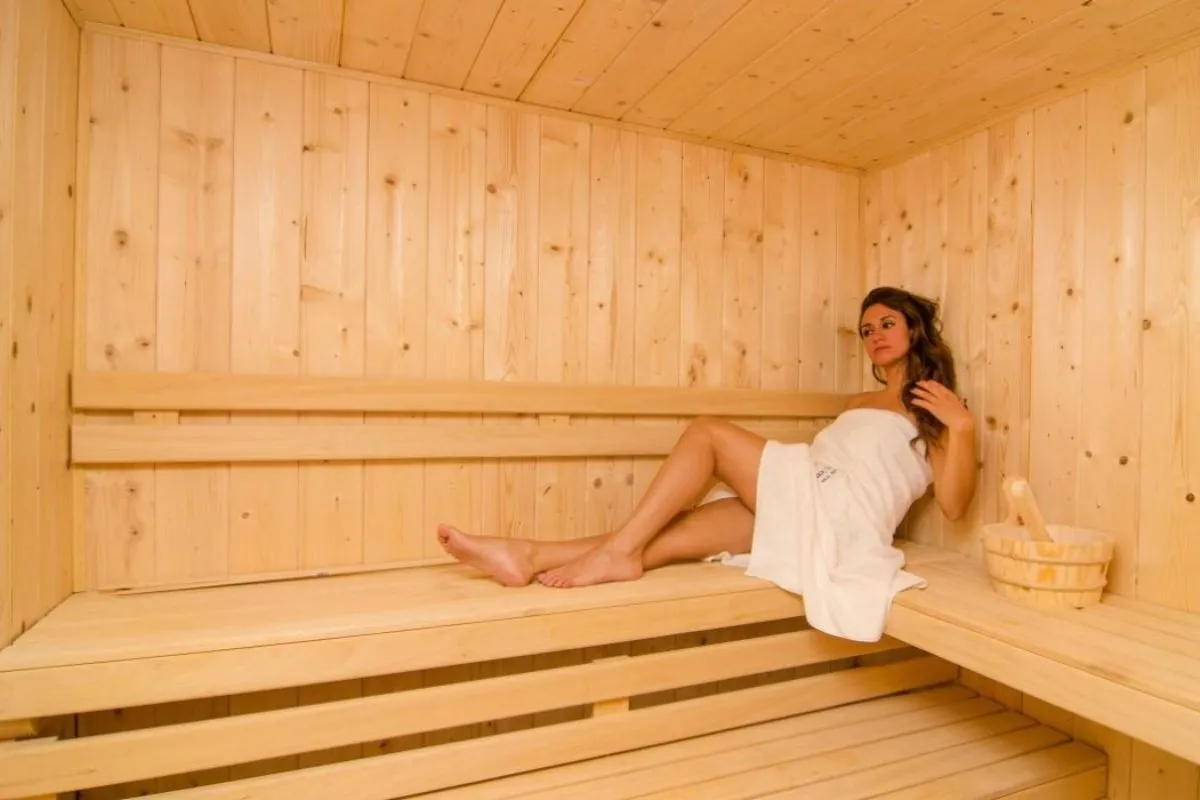 Donna avvolta in un asciugamano bianco seduta all'interno di una sauna in legno chiaro