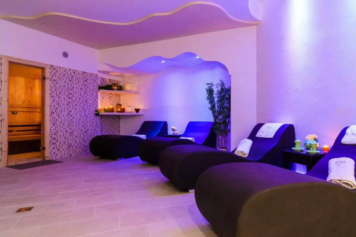 Zona relax della spa con chaise longue, sauna in legno e luci soffuse viola