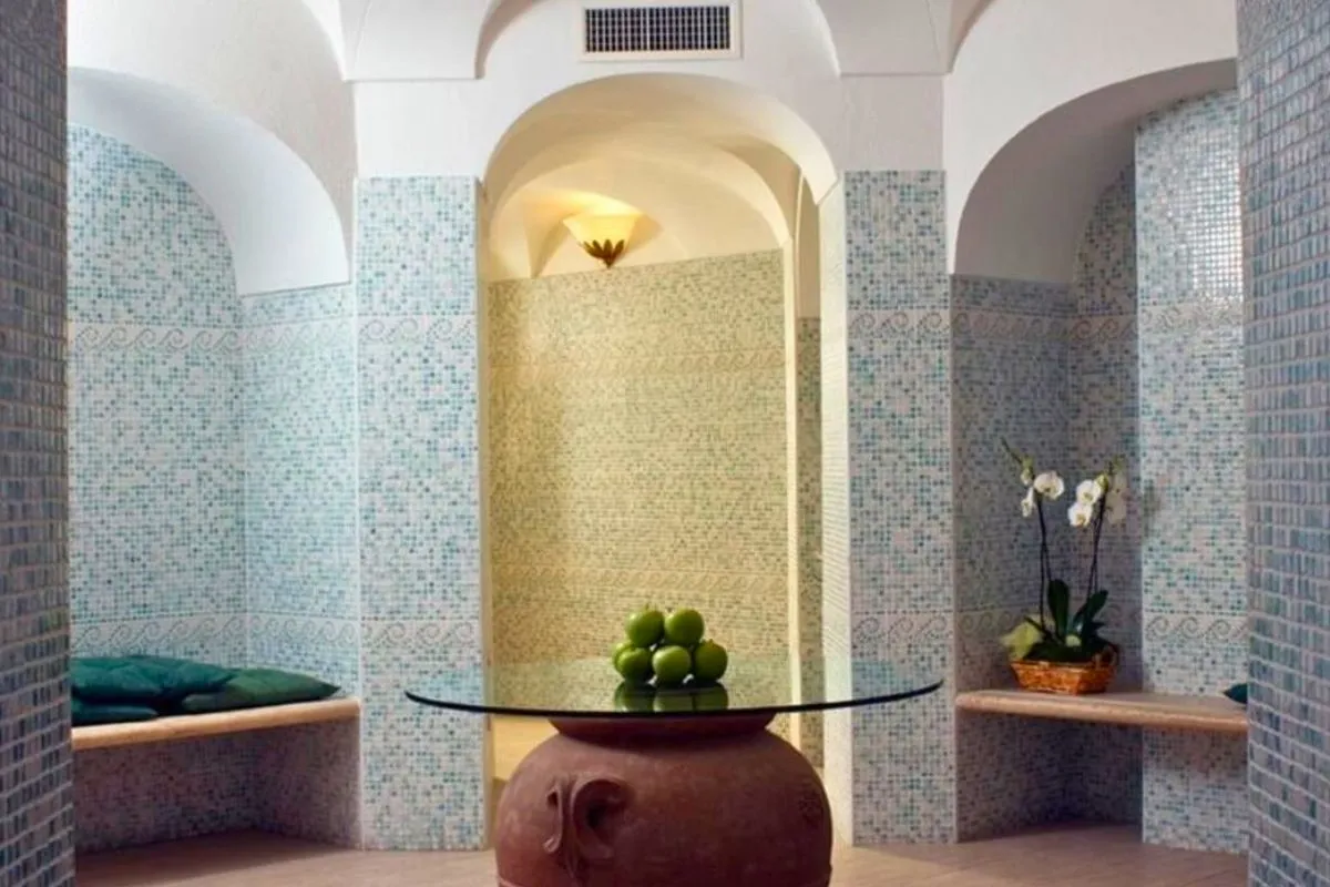 Bagno turco con pareti a mosaico azzurro, nicchie ad arco e anfora in terracotta decorativa