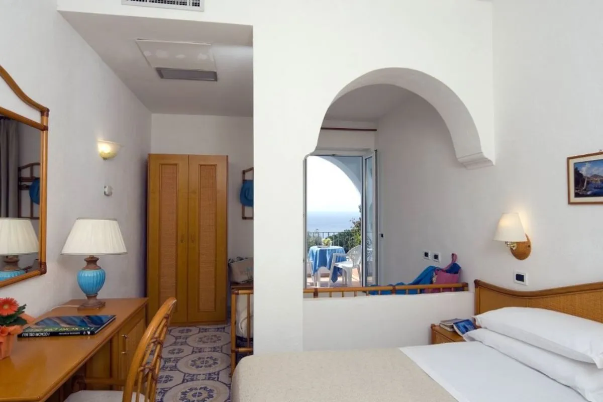 Camera con arco decorativo, scrittoio, armadio in legno e balcone con vista mare