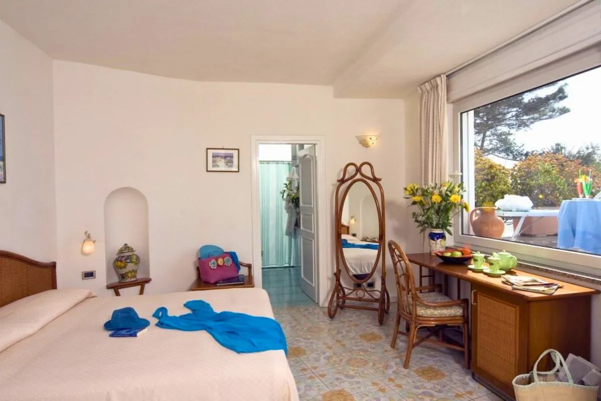 Camera da letto luminosa con letto matrimoniale, specchiera, scrittoio e finestra affacciata sul giardino