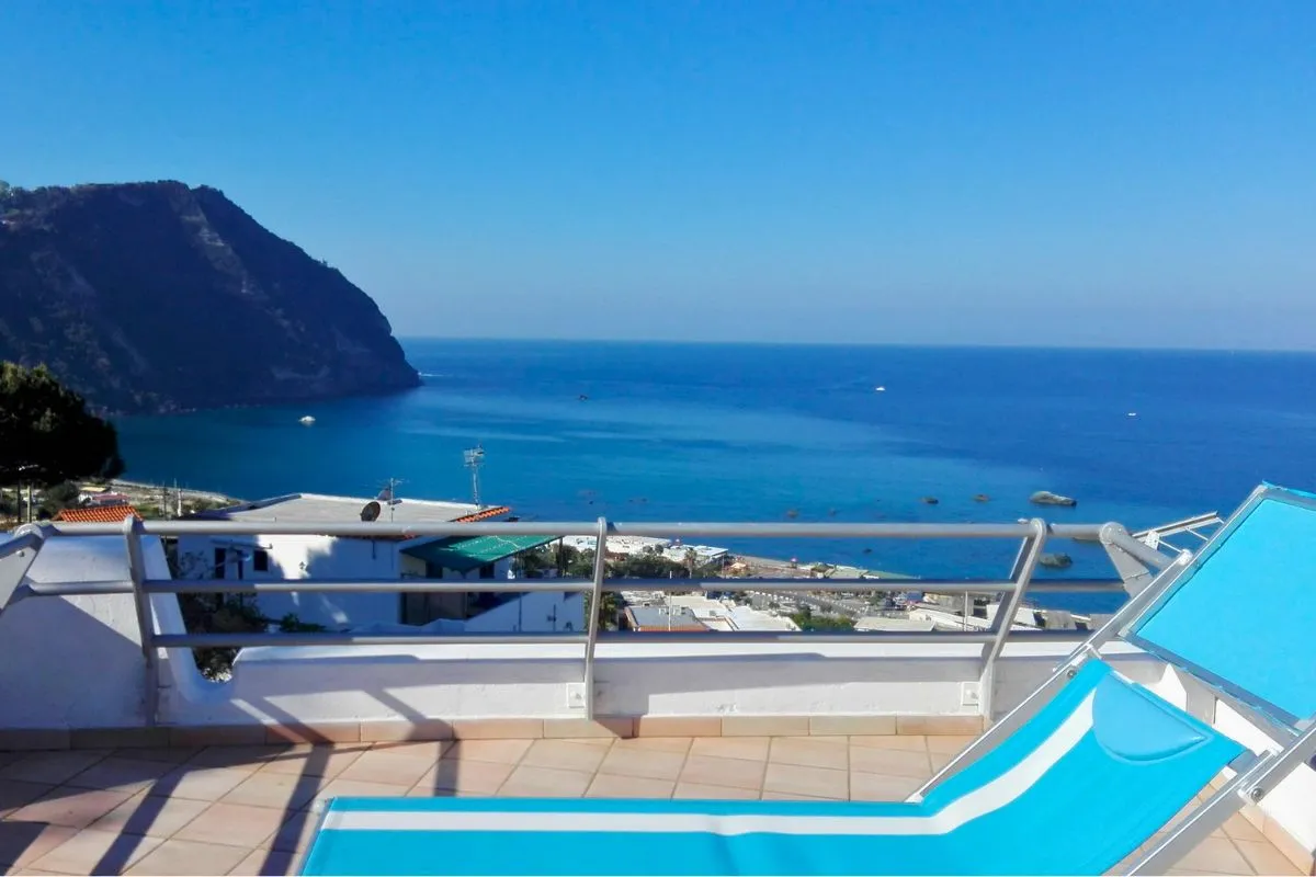 Terrazza con lettino azzurro e vista panoramica sul mare, la baia e il promontorio